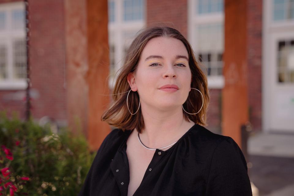 Tori Dunlap wearing a black short-sleeve dress with a necklace, hoop earrings, and yellow eyeliner.