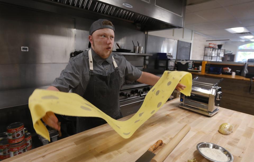 Michael Oldfield rolls a large sheet of laminated egg yolk pasta with edible flowers and chive blossoms at his new M.O. Pasta shop.