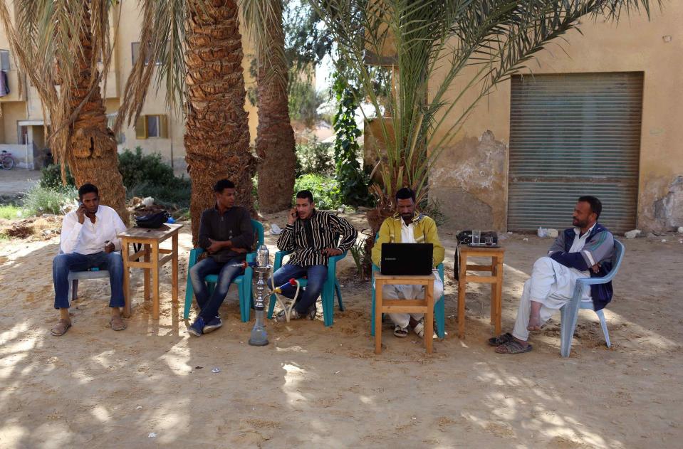 Men smoke and use their mobile phones as they sit at a small cafe in Siwa
