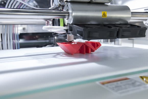 Industrial 3D printer printing an unidentifiable red plastic object.