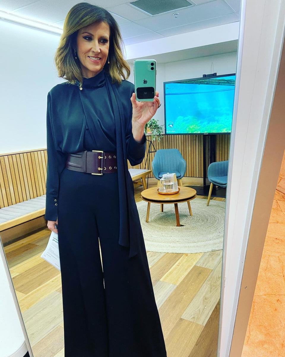 Sunrise host Nat Barr poses for a selfie in front of a large mirror while wearing black pants, a black blouse and a maroon wide belt