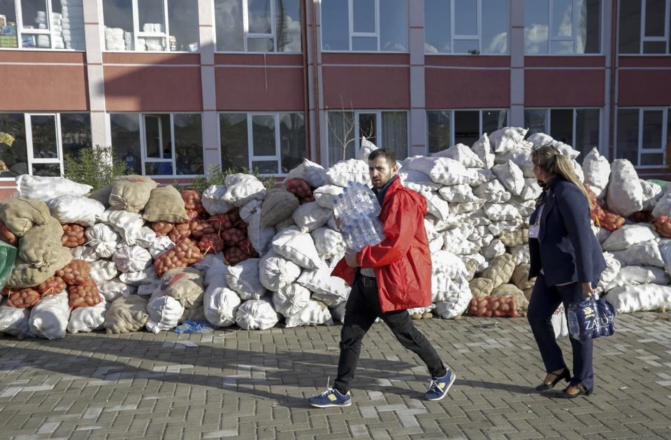 An Albanian couple bottles holds bottles of freshwater as they walk past piles of potatoes stacked at a food collection center, in the town of Durres, western Albania, Saturday, Nov 30, 2019. The search and rescue operation for earthquake survivors in Albania has ended, the prime minister said Saturday, with the death toll at 51 and no more bodies believed to be in the ruins. (AP Photo/Visar Kryeziu)