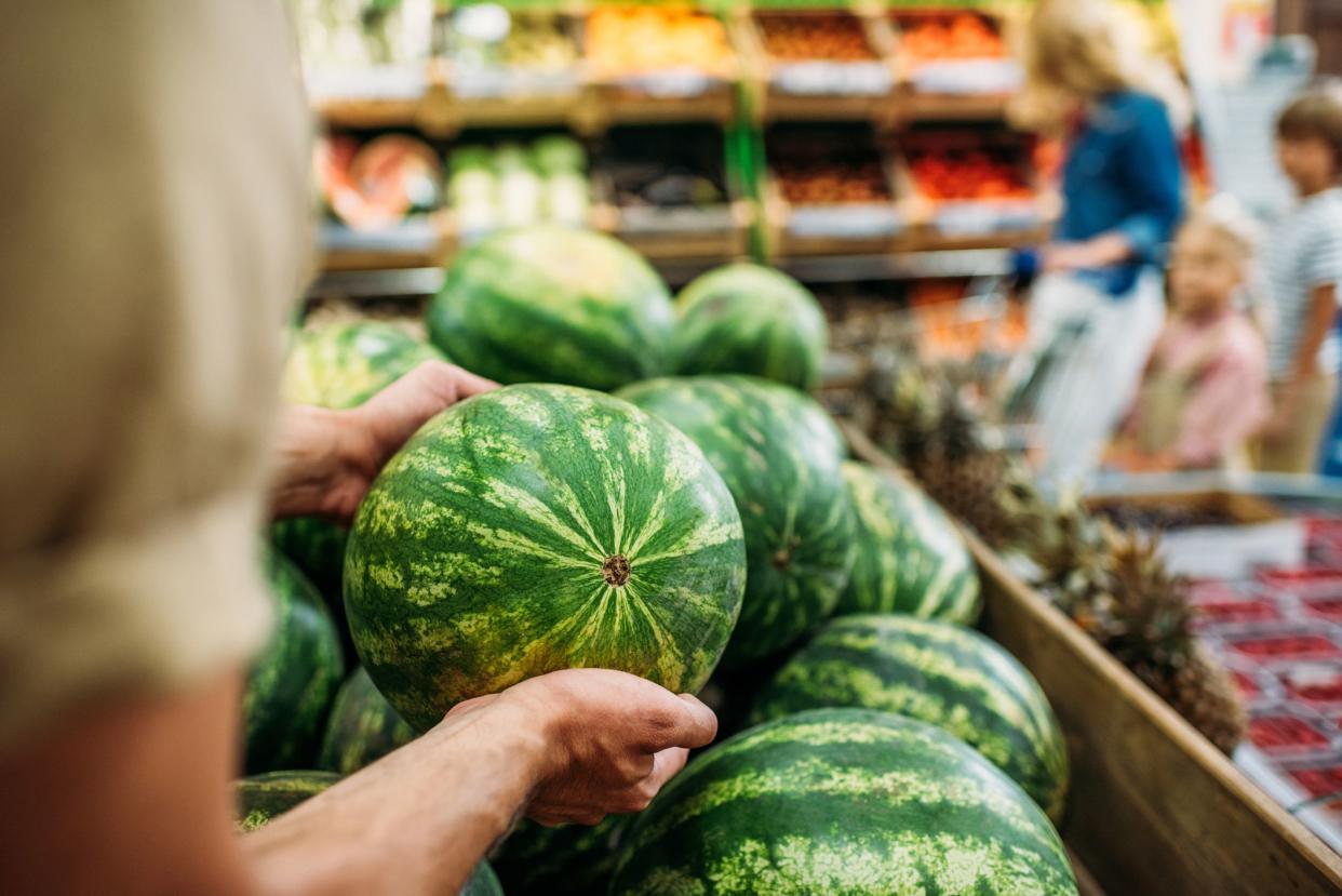 partial view of woman picking watermelon in grocery shop