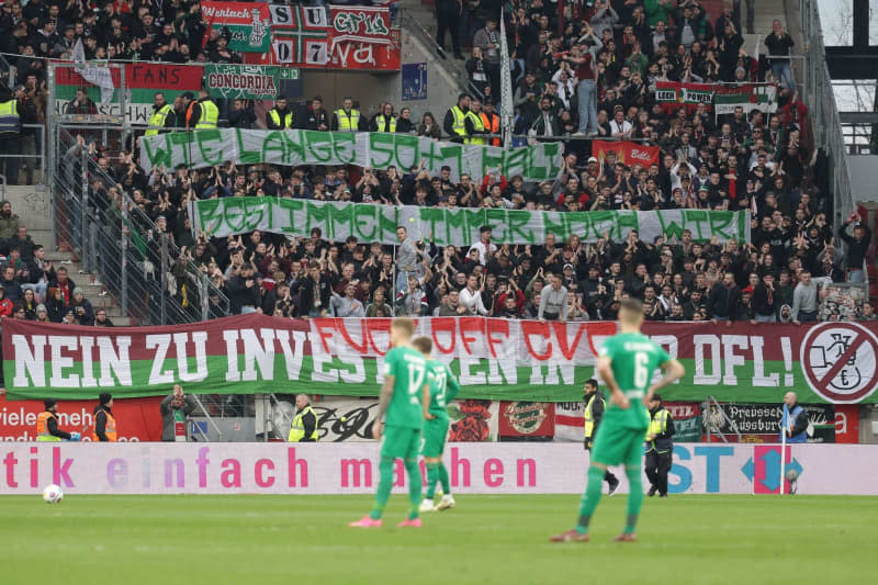 Augsburg fans hold banners reading "How long 50+1 lasts is still up to us" and "No to investors in the DFL" in protest against the German Football League's (DFL) plans to bring in investors, during the German Bundesliga soccer match between FSV Mainz 05 and FC Augsburg at the Mewa Arena. Jürgen Kessler/dpa