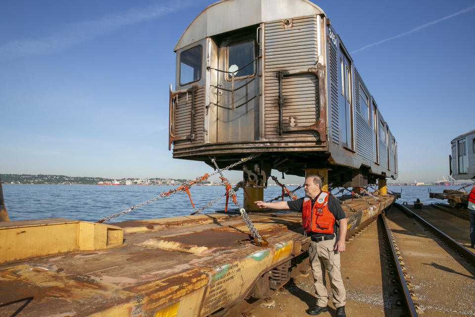 Donald Hutton, director of New York New Jersey Rail for the Port Authority of New York and New Jersey, describes how chains hold a retired 1960s-era R-32 subway train car on a flatcar on a railroad barge as it floats through New York Harbor in New York, on Wednesday, June 15, 2022. Crews are taking the old subway cars to an Ohio scrapyard as the MTA installs new R-179 train cars into the city's sprawling subway system. (AP Photo/Ted Shaffrey)