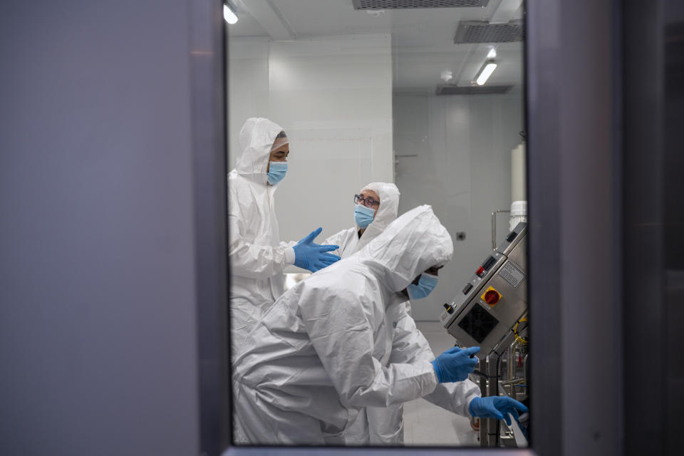 Scientists reenact the calibration of equipment at an Afrigen Biologics and Vaccines facility in Cape Town, South Africa, Tuesday, Oct. 19, 2021. In a pair of warehouses converted into airlocked sterile rooms, young scientists are assembling the equipment needed to reverse engineer a coronavirus vaccine that has yet to reach South Africa and most of the world's poor. ​(AP Photo/Jerome Delay)