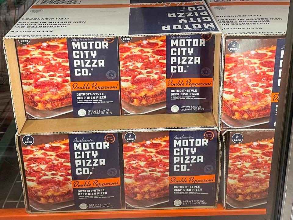 Several boxes with blue labels and images of pepperoni pizzas on them in a freezer section of section