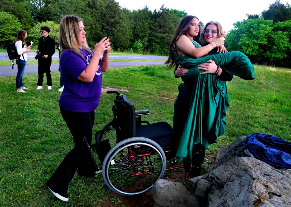 Tucker Moore lifts Janae Edmondson out of her wheelchair during pre-prom photos on a rock at The Stones River Battlefield on April 29, 2023.