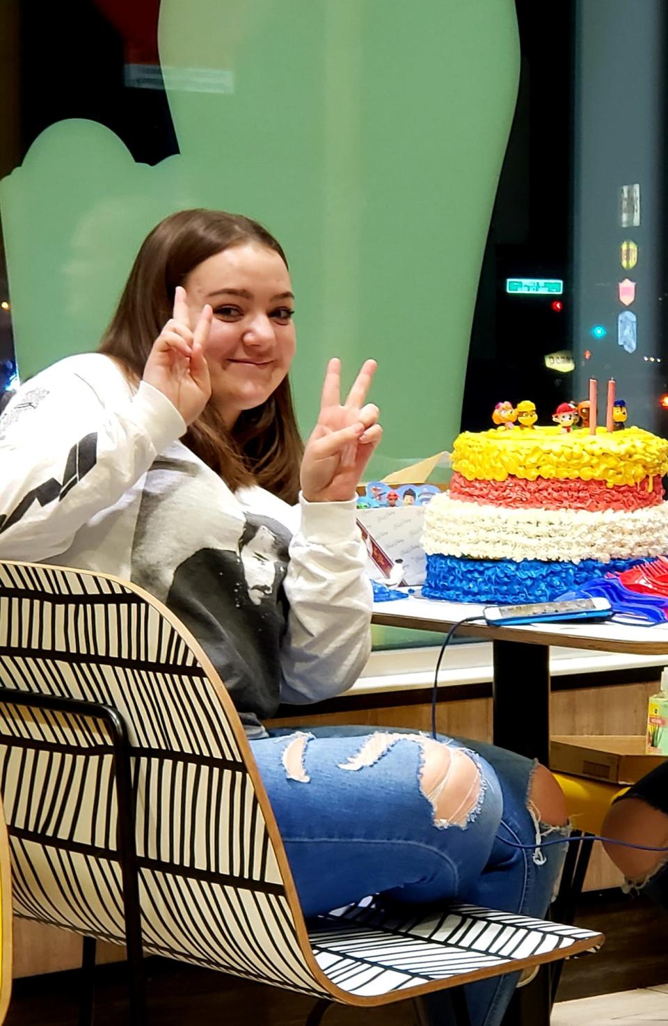 Kylie Leniz, who was fatally shot while working at McDonald's, smiles and holds up two peace signs with a cake.