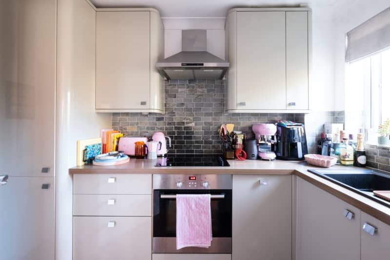 Pink accessories sit atop oven and white cabinetry in kitchen.