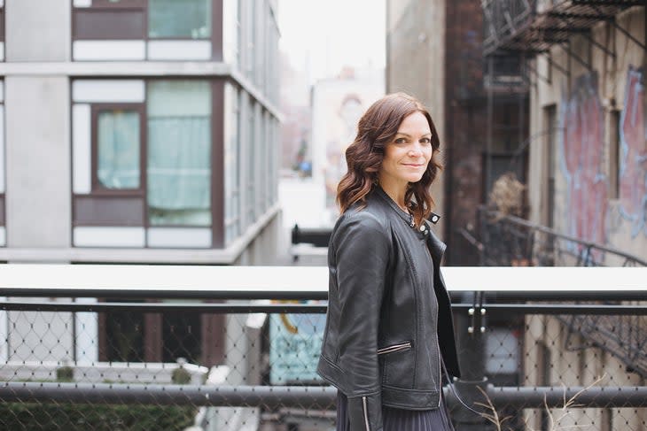 Kerri Kelly in black jacket stands among city buildings