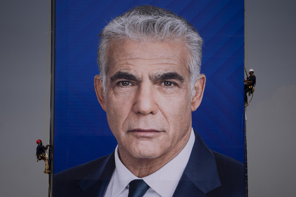 File - Workers hang an election campaign billboard showing Israeli Prime Minister and the head of the Yesh Atid party Yair Lapid, in Ramat Hasharon, Israel, Sunday, Oct. 23, 2022. Israel is heading into its fifth election in under four years on Nov. 1. (AP Photo/Oded Balilty, File)