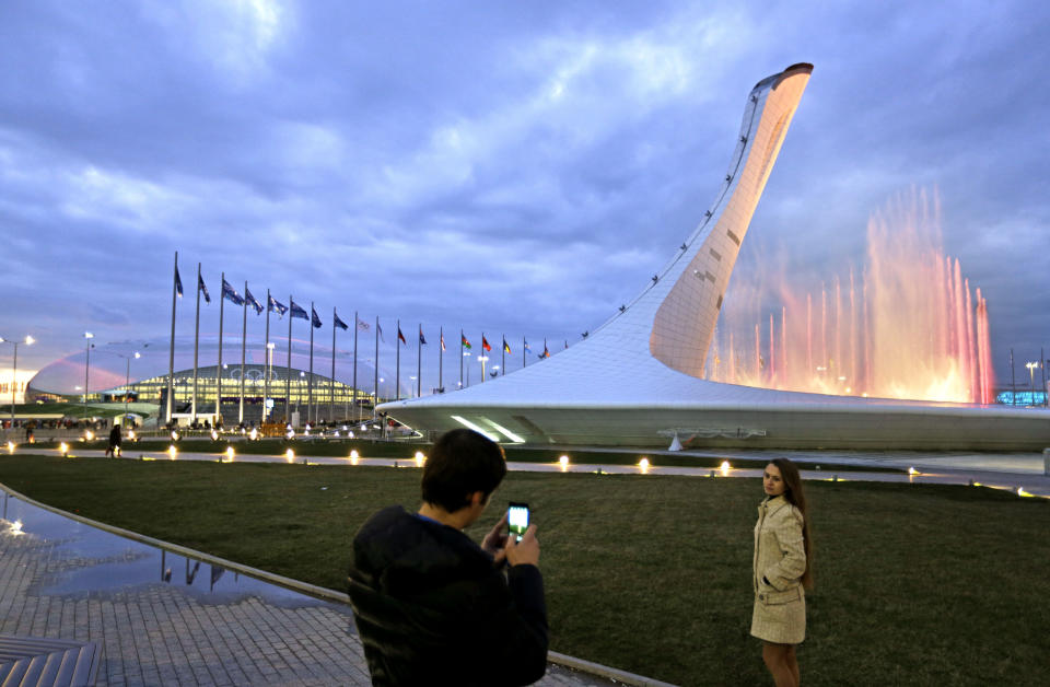 A couple takes a picture during the testing of a water light show at the Olympic cauldron as the Bolshoy Ice Dome stands at left at the 2014 Winter Olympics, Saturday, Feb. 1, 2014, in Sochi, Russia. (AP Photo/David Goldman)