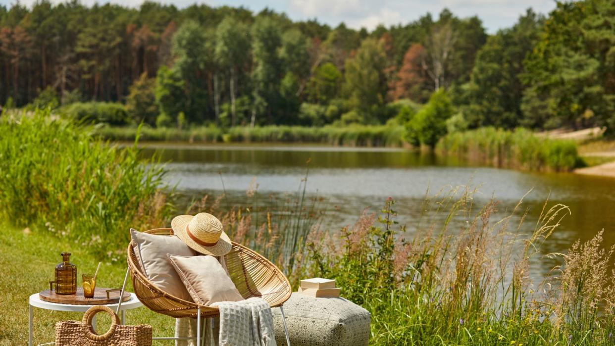 stylish composition of outdoor garden on the lake with design rattan armchair and elegant accessories summer chillout mood