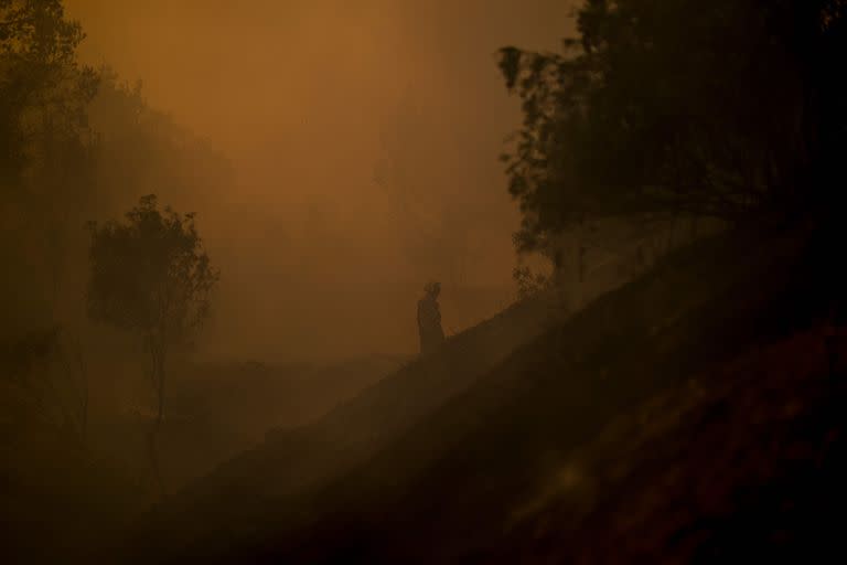 Un bombero permanece parado en medio del intenso humo provocado por los incendios
