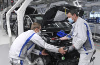 Max Bruehmann (l) and Heiko Gruner employees of German car producer Volkswagen Sachsen, work with face masks in the assembly of the ID.3 in the vehicle plant in Zwickau, Germany, Thursday, April 23, 2020. At carmaker Volkswagen, vehicle production restarts after a corona shutdown of more than five weeks. Production of the all-electric ID.3 will initially be restarted with reduced capacity and cycle time. Zwickau is the first VW vehicle plant in Germany to resume operations. (Hendrik Schmidt/dpa via AP)