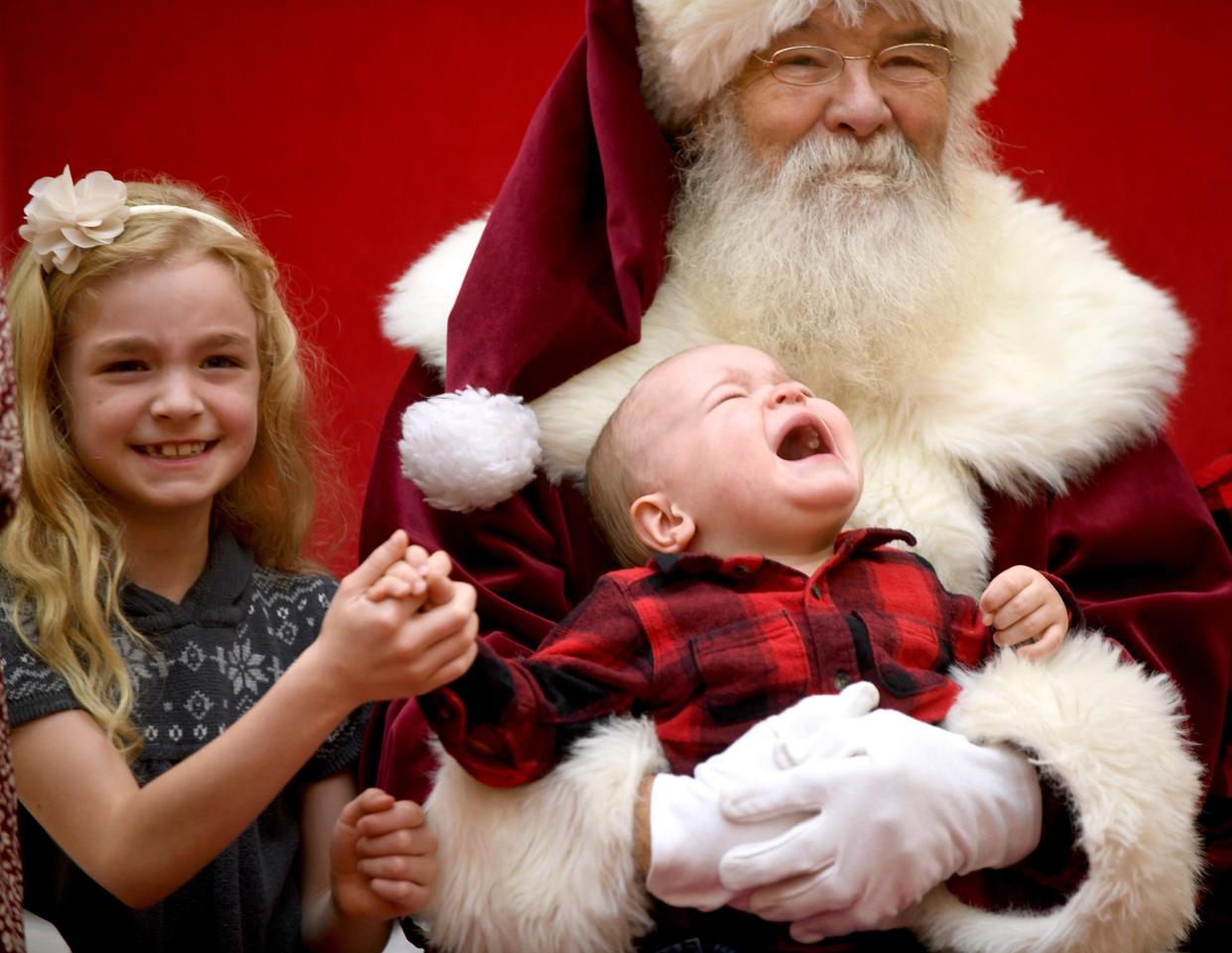 Lucy Wineka, 7, of North Canton does her best to reassure her cousin, Chance Koteles, 1, of North Canton during a visit to see Santa, who got an assist from Bernie Roberts of Akron at the Belden Village Mall.