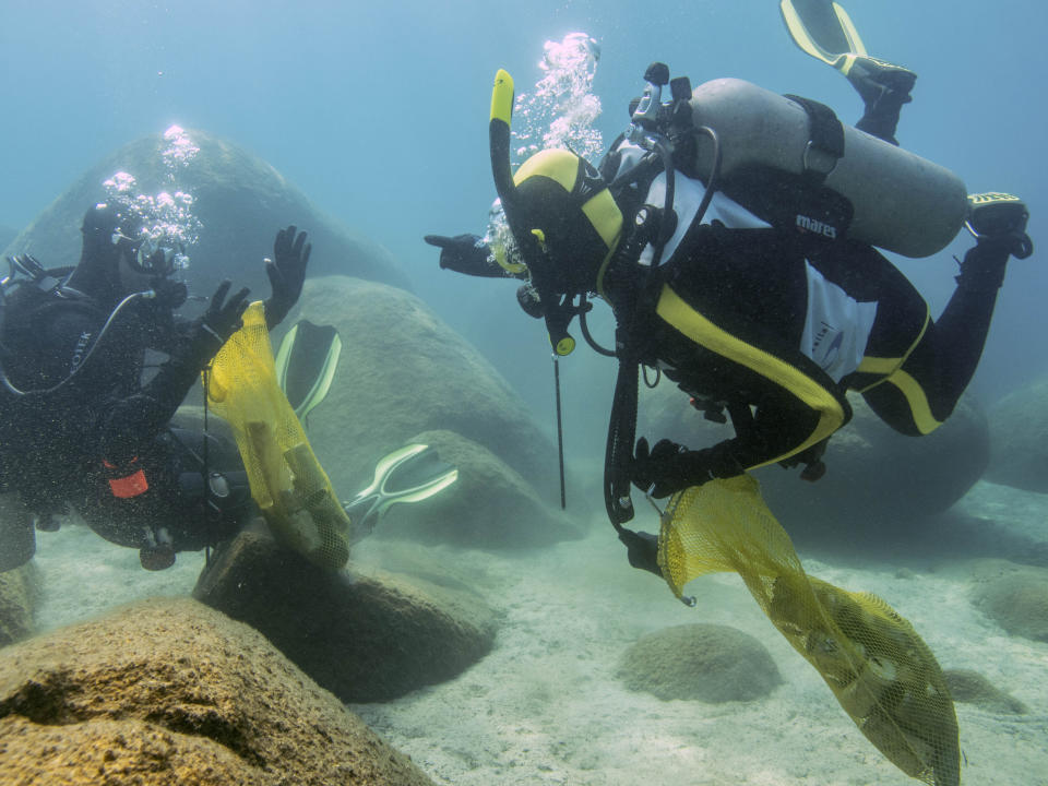 This photo provided by Clean Up The Lake shows a scuba divers beneath the surface of Lake Tahoe, cleaning up trash on Friday, May 14, 2021. A team of scuba divers on Friday completed the first dive of a massive, six-month effort to rid the popular Lake Tahoe of fishing rods, tires, aluminum cans, beer bottles and other trash accumulating underwater. (Clean Up The Lake via AP)