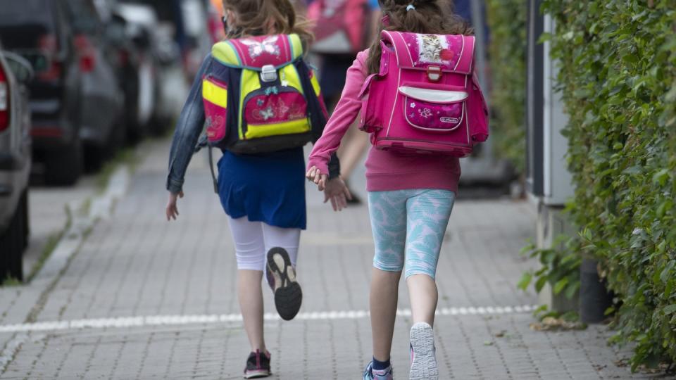 Zwei Schülerinnen einer Grundschule rennen mit einem Schulranzen auf dem Rücken die letzten Meter bis zum Schulhof.