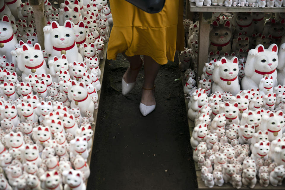 In this June 25, 2019, photo, a tourist walk between beckoning cat figurines after posing for photos with them at Gotokuji Temple in Tokyo. According to a centuries-old legend provided by the temple, Gotokuji, a Buddhist temple located in the quiet neighborhood of Setagaya, is the birthplace of beckoning cats, the famous cat figurines that are widely believed to bring good luck and prosperity to home and businesses. Some visitors come just to snap a few photos, while others make a trip to the temple to pray and make wishes. (AP Photo/Jae C. Hong)