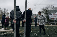Local residents look at two alleged collaborators tied by the hands to pillars in Kherson, Ukraine, Sunday, Nov. 13, 2022. Residents of Kherson celebrated the end of Russia’s eight-month occupation for the third straight day Sunday, even as they took stock of the extensive damage left behind in the southern Ukrainian city by the Kremlin’s retreating forces. (AP Photo/LIBKOS)
