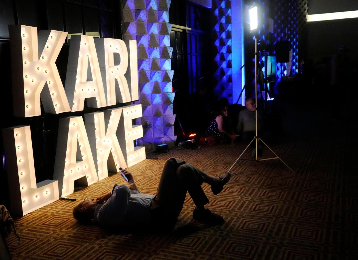 Curt Bruggman looks at his phone in front of a sign for Arizona Republican gubernatorial candidate Kari Lake during an election night party in Scottsdale on Aug 2, 2022.