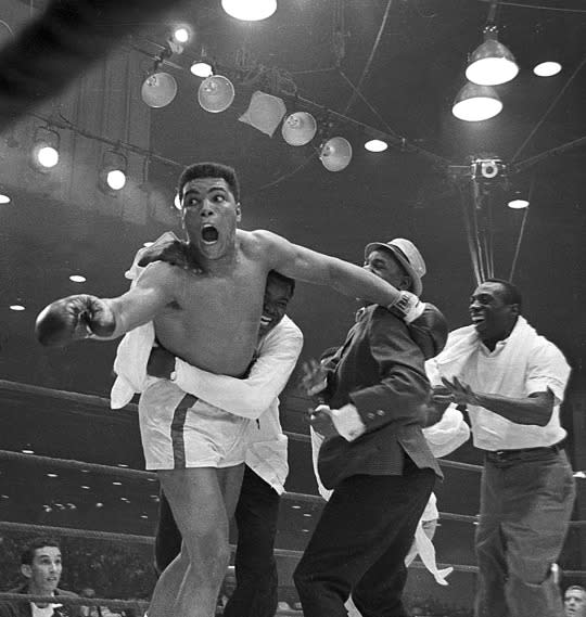 <p>Cassius Clay’s handlers hold him back as he reacts after he is announced the new heavyweight champion of the world on a seventh round technical knockout against Sonny Liston at Convention Hall in Miami Beach, Fla., on Feb. 25, 1964. (AP Photo)</p>