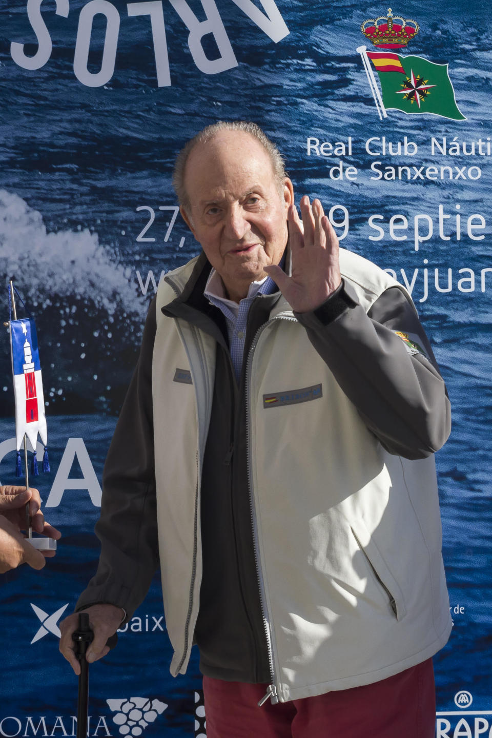 King Juan Carlos I of Spain dressed in a vest and jumper holding a walking stick at a sailing club in Spain
