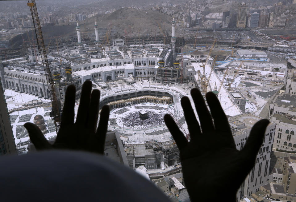 A Muslim prays from a hotel overlooking the Kaaba, the cubic building at the Grand Mosque, in the Muslim holy city of Mecca, Saudi Arabia, Wednesday, March 4, 2020. On Wednesday, Saudi Arabia's Deputy Health Minister Abdel-Fattah Mashat was quoted on the state-linked news site Al-Yaum saying that groups of visitors to Mecca from inside the country would now also be barred from performing the pilgrimage, known as the umrah. (AP Photo/Amr Nabil)
