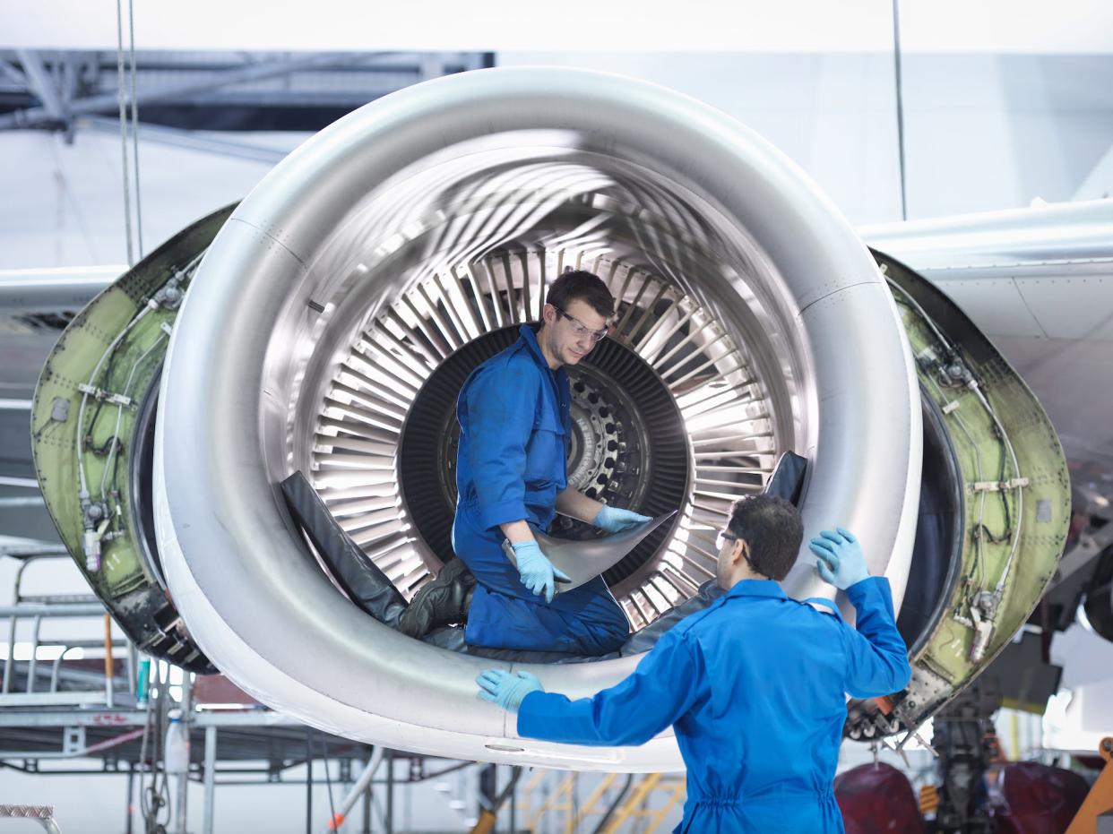 Engineers working with jet engine turbine blade in aircraft maintenance factory.