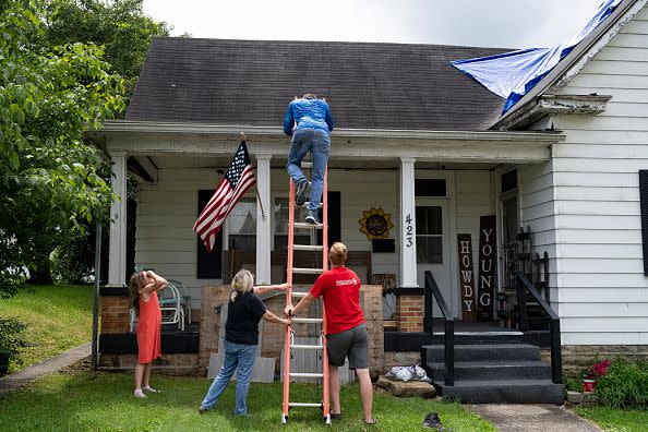 Brandon Hayes, 32, climbs down from a ladder after hammering a tarp onto the roof of a neighbor on July 28, 2022, in Jackson, Kentucky.