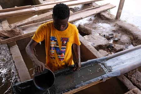 An informal gold miner pours water over ground-up rock at an angle to wash the heavier gold elements to the bottom at a site in Bawdie