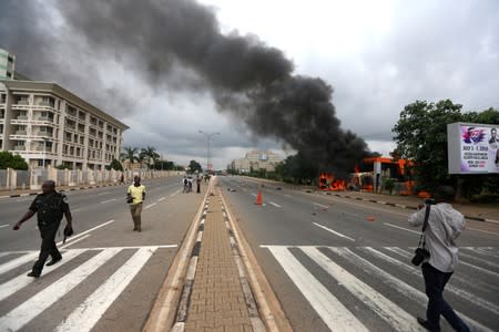 A police officer walks past a photographer after the Shi'ite group set an ambulance and a fire engine on fire at the Federal Secretariat in Abuja