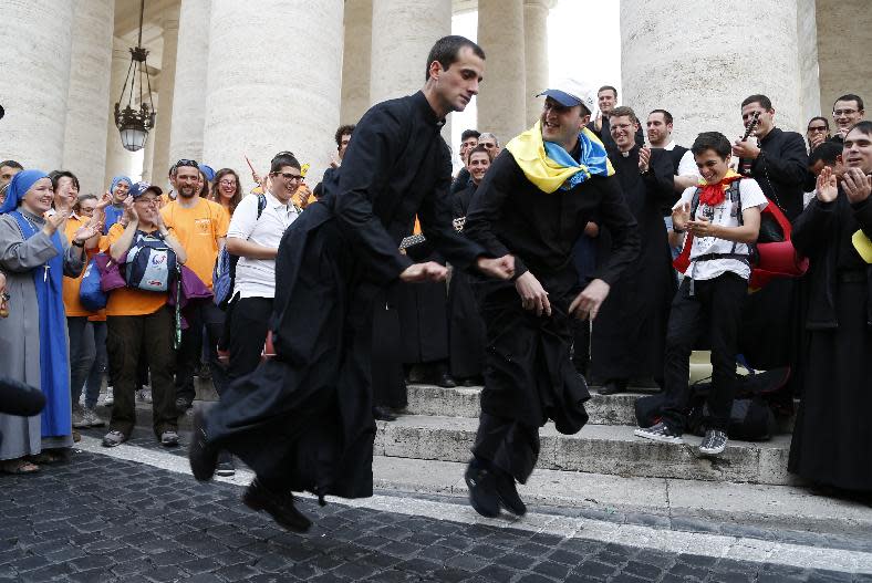 Two priests, one of them with an Ukrainian flag on his shoulders, dance in St. Peter's Square at the Vatican, Saturday, April 26, 2014. Pilgrims and faithful are gathering in Rome to attend Sunday's ceremony at the Vatican where Pope Francis will elevate in a solemn ceremony John XXIII and John Paul II to sainthood. (AP Photo/Domenico Stinellis)