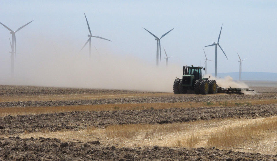 A farmer plows a field near wind turbines owned by Chicago-based Exelon Corp. outside of Mountain Home, Idaho on Thursday, Aug. 2, 2012. State electricity regulators aiming to set the course for Idaho's renewables industry for years to come will hold hearings next week on long-running and bitter disputes between utilities like Idaho Power Co. and independent wind, solar and biogas developers. The Idaho Public Utilities Commission has scheduled three days of hearings starting Tuesday, to be attended by a crowd of lawyers, utility executives and environmentalists. (AP Photo/John Miller)