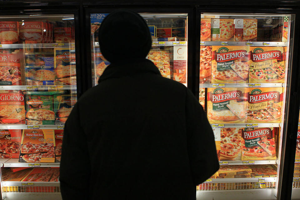 Person standing in front of a freezer full of boxed pizzas in a store