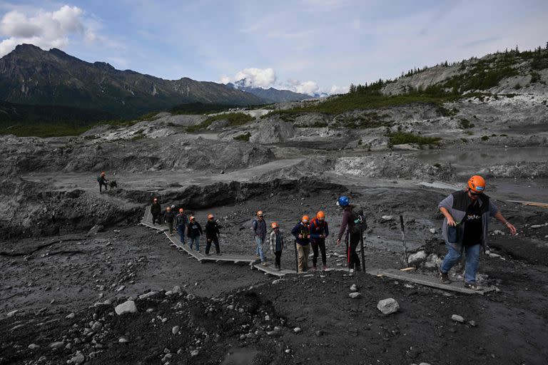 Grupos de visitantes caminan sobre un puente improvisado a través de una morrena glacial. Las morrenas se generan por el transporte y deposición de sedimentos en los márgenes del hielo