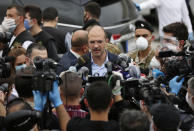 In this Sunday, April 5, 2020, Lebanese Health Minister Hamad Hassan, center, ignoring social distancing rules and not wearing mask, speaks with journalists during the arrival of Lebanese passengers who were stuck in Saudi Arabia and other countries because of the coronavirus outbreak, outside Rafik Hariri Airport, in Beirut. From the U.S. president to the British prime minister's top aide and far beyond, leading officials around the world are refusing to wear masks or breaking confinement rules meant to protect their populations from the coronavirus and slow the pandemic. While some are punished when they're caught, or publicly repent, others shrug off the violations as if the rules don't apply to them. (AP Photo/Hussein Malla)