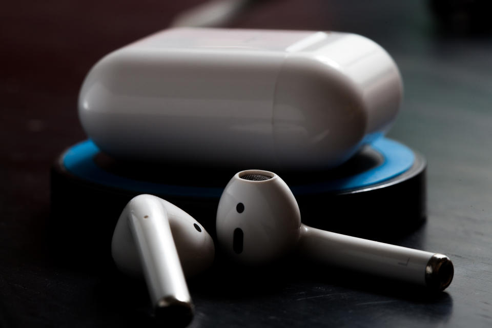 both Airpods and charging case on a wireless charger photographed on a dark table in lowkey light