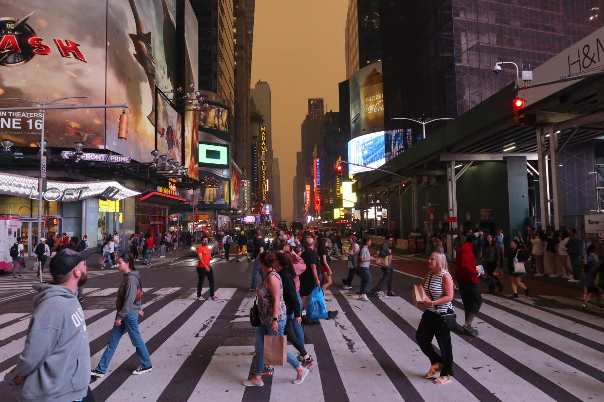 People walk across a busy street while a smoky sky can be seen in the background.