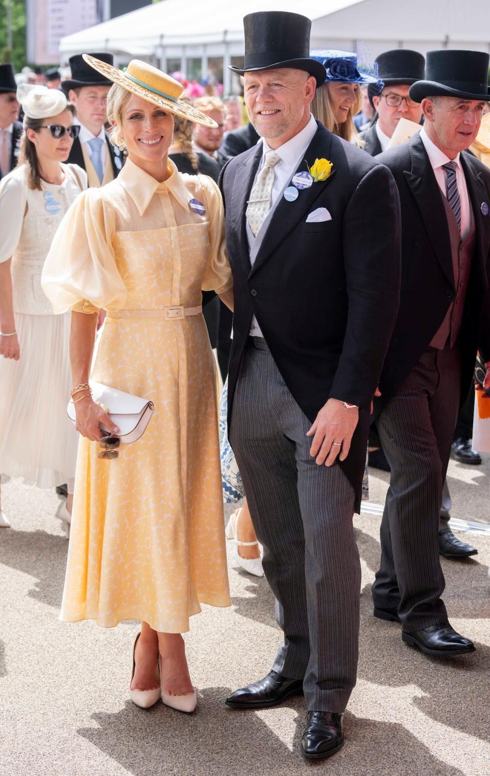 Zara Tindall posing in a yellow dress alongside her husband Mike Tindall, who is wearing a black and gray morning suit.