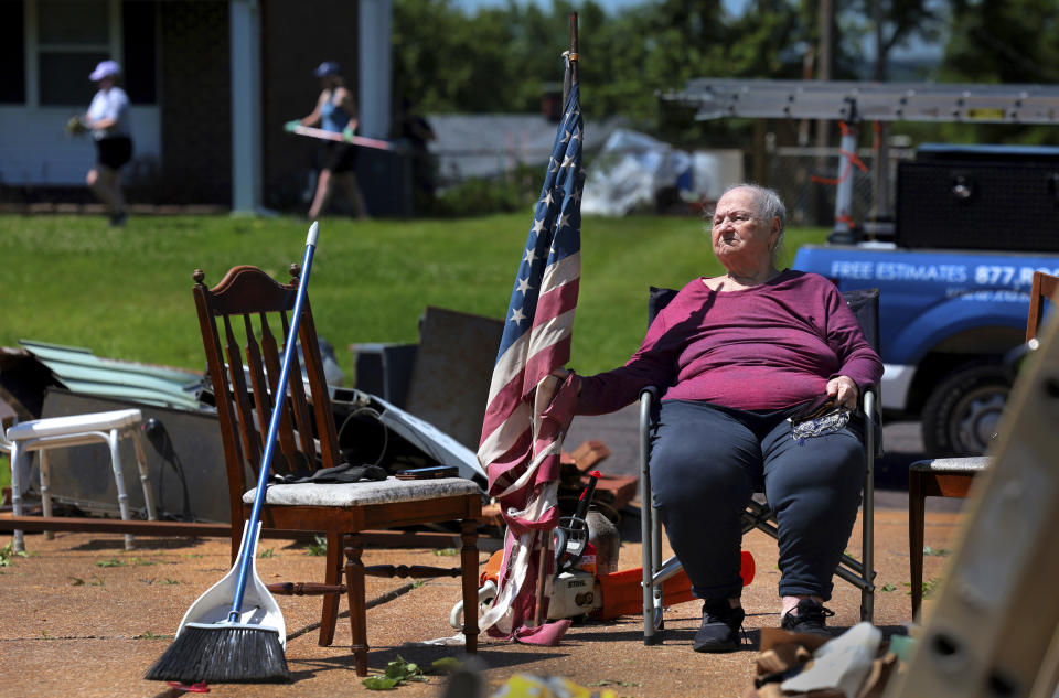 Jackie Moloney, 88, hangs on to her shredded American flag on Monday, May 27, 2024 as her family cleans up on Morningdale Place in Mehlville, Mo. following a violent storm and possible tornado that hit Sunday evening. The storm destroyed her garage and sent part of a neighbor's roof into her backyard. Moloney's daughter Patti Manley got her up and into an interior bathroom as the storm hit. "We heard a loud whoosh," said Monloney, who bought her home new in 1965. "Thank God for family." (Robert Cohen/St. Louis Post-Dispatch via AP)