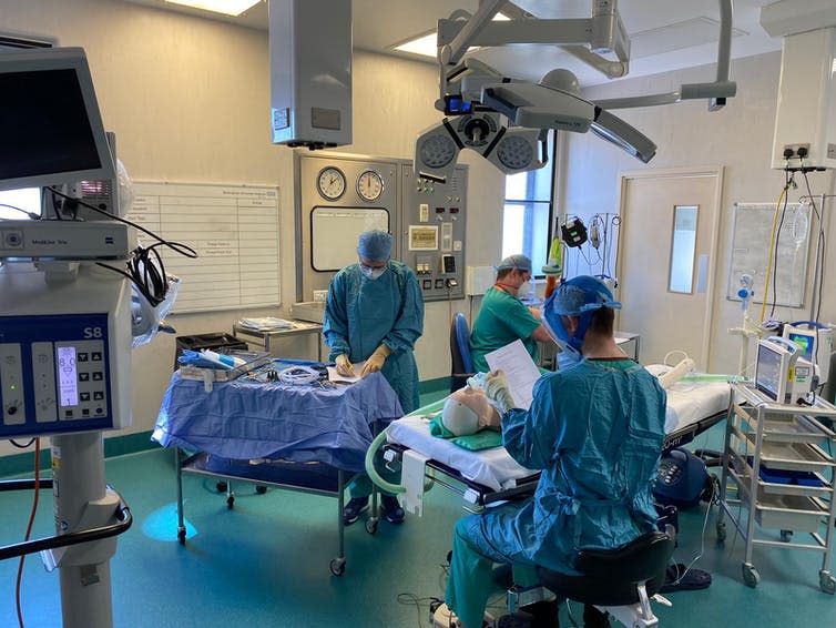 Three people wearing surgical scrubs in an operating theatre.