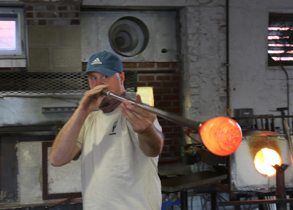 Benjamin Giguere blows through a tube to shape molten glass at his Gather Glass studio in Providence, where you can learn the art and bring home a handmade treasure.