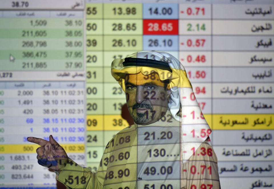 A trader talks to others in front of a screen displaying Saudi stock market values at the Arab National Bank in Riyadh, Saudi Arabia, Thursday, Dec. 12, 2019. Shares in Saudi Aramco gained on the second day of trading Thursday, propelling the oil and gas company to a more than $2 trillion valuation where it holds the title of the world's most valuable listed company. (AP Photo/Amr Nabil)