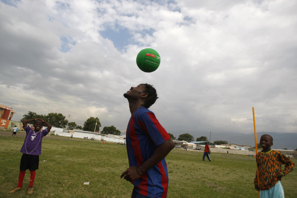 In this May 17, 2012 photo, soccer coach Rejouis Gachelin controls the ball as young players look on in a field that is part of the L'Athletique D'Haiti sports program at the northeastern edge of Cite Soleil, in Port-au-Prince, Haiti. A local sports hero, a New York real estate developer and a well-known architect are teaming up to build a soccer stadium in Cite Soleil, hoping to revive the seaside shantytown. The organizers also hope the stadium, scheduled to break ground within six months and due to be built by the end of 2013, will bring an initial 500 jobs and inject commerce into the shanty city, where politicians to pay residents to fight their battles as proxy forces. (AP Photo/Dieu Nalio Chery)