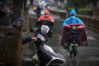 People wearing face masks to protect against the coronavirus ride scooters during a rainfall in Beijing, Wednesday, Aug. 5, 2020. Measures to contain the spread on a COVID-19 outbreak in China's northwestern region of Xinjiang, including locking down some communities and limiting public transport, appear to have been effective and reported case numbers have gradually fallen. (AP Photo/Mark Schiefelbein)