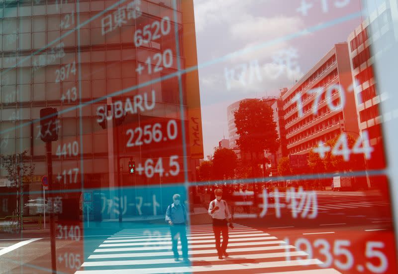 People wearing protective masks, following the coronavirus disease (COVID-19) outbreak, are reflected on a screen showing stock prices outside a brokerage in Tokyo