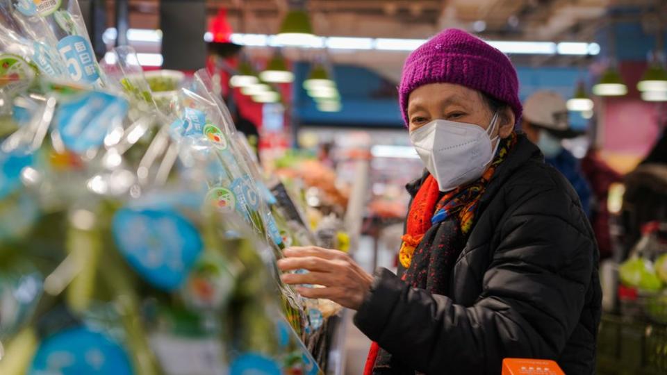 北京一位老人在菜市場內戴著口罩選購青菜（10/2/2023）