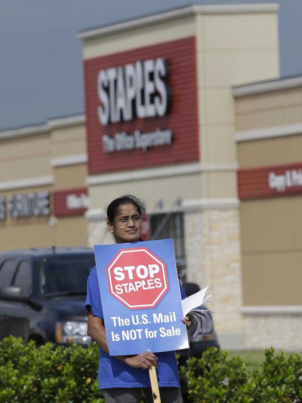 Postal worker Sophia Joseph holds a sign outside a Staples store during a protest in Dallas, Thursday, April 24, 2014. Thousands of postal workers around the nation are expected to picket outside Staples' stores to protest a pilot program of postal counters in the stores that are staffed with Staples employees. (AP Photo/LM Otero)